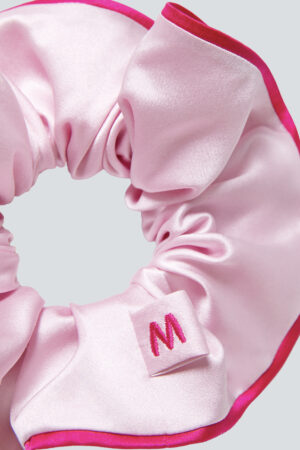 Close-up of a Macaron Large Silk Scrunchie in pink with a contrasting red edge and embroidered M logo.