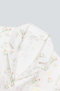 Elegant collar detail of a silky pajama set with the 'mamito' logo and soft floral sketches.