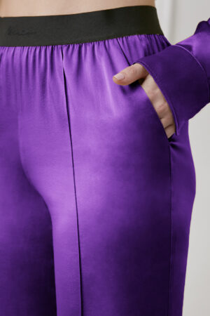 Close-up of purple Vibrant Silk Pants pocket and black elastic waistband with hand in pocket.