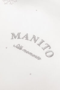 Close-up of MANITO's signature monogram, 'Silk Moments', representing the brand's dedication to bespoke silk elegance.