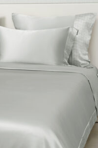 Aether bedding collection featuring charmeuse silk fabric and plaid edge details in soft quartz gray tone.