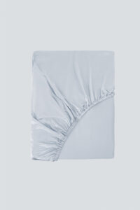 Folded MANITO Authentic Silk Fitted Sheet in light blue, highlighting its elegant sheen and corner stitching.
