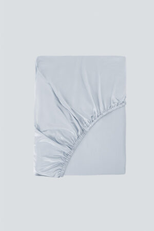 Folded MANITO Authentic Silk Fitted Sheet in light blue, highlighting its elegant sheen and corner stitching.