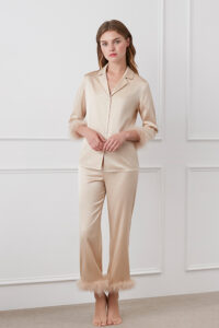 Full view of champagne MANITO Diva Feather Trimmed Pajama Set, model standing barefoot against white panel wall.