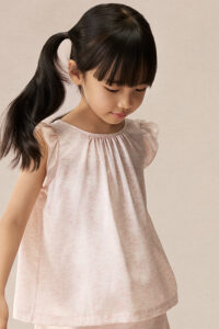 Girl wearing BONPOINT×MANITO Ailette Kid's Pajama Set Gift Box with flutter-sleeve silk top and matching pink floral shorts.