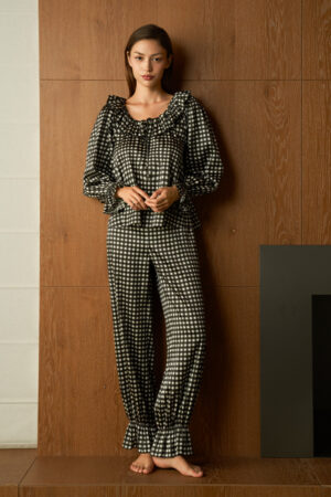 Full view of woman in black Blooming Women's Pajama Set, standing barefoot by the fireplace in an easy, lounging pose.