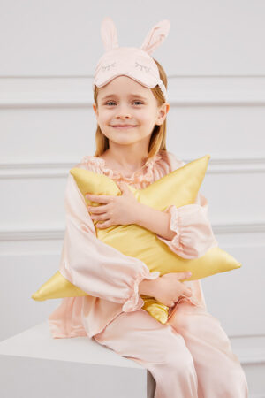 Child hugs yellow star pillow while wearing Bunny Child Eye Mask with playful rabbit design.