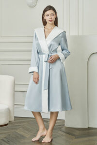 Woman wears Calla Women's Hooded Bathrobe in baby blue silk, exuding soft morning elegance and effortless comfort.