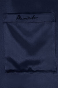 Detailed view of MANITO embroidered logo on the chest pocket of the Chemise Mashinen navy silk pajama shirt.