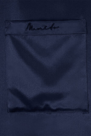 Detailed view of MANITO embroidered logo on the chest pocket of the Chemise Mashinen navy silk pajama shirt.