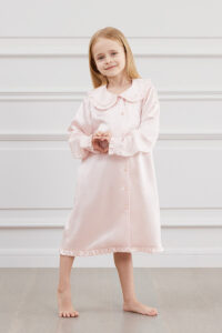 A girl in MANITO Pink Cloud Silk Nightgown with ruffled trim and pipped lapels.