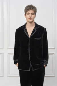 Man wears Combo Velvet Pajama Set in black, standing relaxed with hands in pockets and satin-trimmed collar showing.