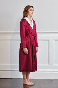 Graceful woman in a luxurious red silk terry robe with white trim, embodying opulence and relaxation.