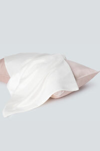 Elegant set of silk pillowcases in white and pink, placed on a soft surface conveying a sense of luxury and comfort.