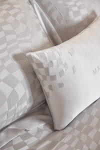 Close-up of Damier Silk Duvet Cover with satin pillow featuring abstract chessboard design and the brand's logo.
