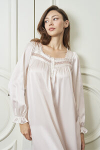 Woman wears Dream Women's Nightdress in soft pink silk, highlighting the delicate lace-trimmed neckline and gentle sheen.