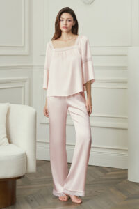 Woman wears MANITO Dream Women's Pajama Set in pink silk, standing gracefully, embodying relaxed elegance.