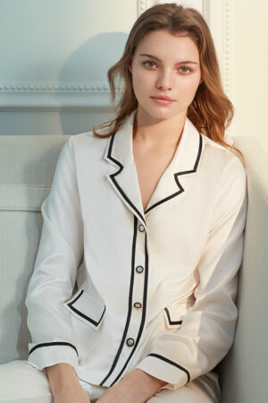 Elegant woman in a Coco Lady silk pajama set with black piping and button-down shirt.