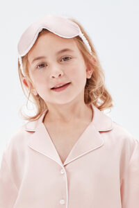A child wearing a soft pink silk pajama set and matching silk eye mask.