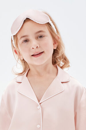 A child wearing a soft pink silk pajama set and matching silk eye mask.