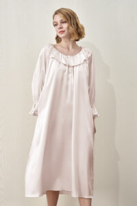 A female model wearing MANITO Echoes Silk Ruffle Dress in pink, featuring ruffle neckline and a loose, elegant fit.