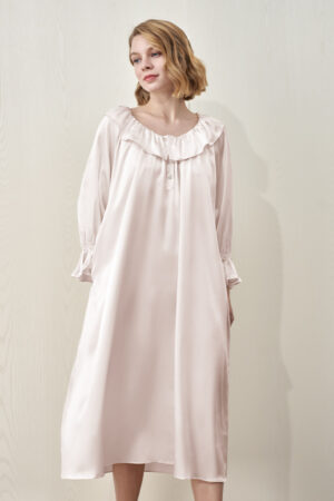 A female model wearing MANITO Echoes Silk Ruffle Dress in pink, featuring ruffle neckline and a loose, elegant fit.