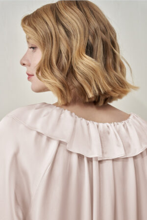 Back close-up view of the female model in pink MANITO Echoes Silk Ruffle Dress, showing the soft folds and ruffle collar detail.