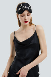Woman wears MANITO Pearlwear Silk Eye Mask with pearl logo design, reflecting modern sophistication.