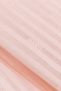 Detail shot of MANITO Faery pajama fabric showing tonal stripe weave and brand logo.