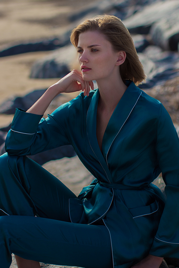 A woman reclining on rocks, wearing the Elite Women's Silk Robe Suit, with thoughtful pose.