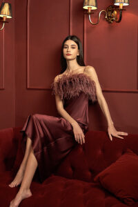 A model in Fiesta red feather-adorned silk nightdress, seated gracefully.