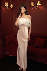 A model in Fiesta pink feather-trimmed silk nightdress, poised against a rich red backdrop.