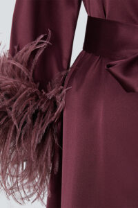 Close-up of feather cuffs on a red charmeuse silk long robe, adding a sophisticated holiday touch.