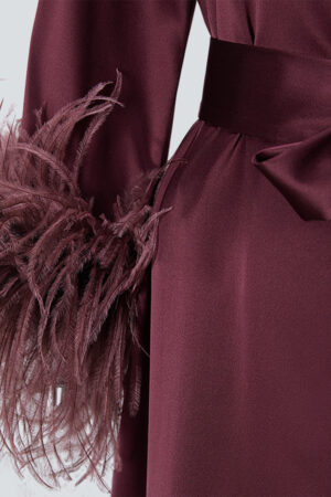 Close-up of feather cuffs on a red charmeuse silk long robe, adding a sophisticated holiday touch.