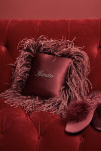 Red throw cushion with holiday-themed feathers and sparkling rhinestones on a luxurious velvet sofa.