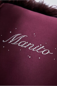 Close-up of rhinestone-embellished MANITO logo on a red throw cushion, showcasing fine craftsmanship.