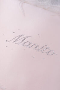 Detailed view of rhinestone accents on a pink throw cushion with a soft satin finish.