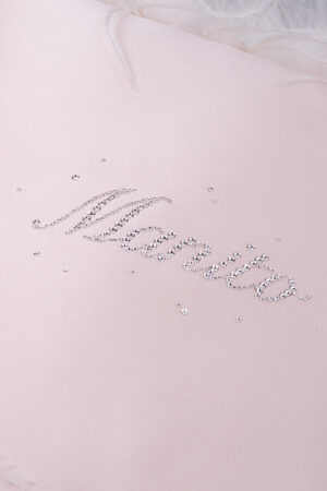 Detailed view of rhinestone accents on a pink throw cushion with a soft satin finish.