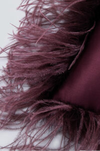 Elegant maroon feathers on a luxurious red holiday throw pillow, highlighting festive design.