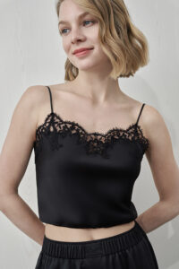 Model wearing MANITO Flora Lace Silk Camisole Top in black, featuring a bold neckline on a classic black silk lace top.