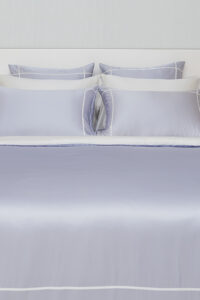 MANITO Fluora Silk Pillowcase Set on a made-up bed, featuring layered color contrasts in lavender and white.