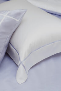 Close-up of MANITO Fluora Silk Pillowcase in white with soft lavender piping, highlighting the elegant stitching and silky texture.