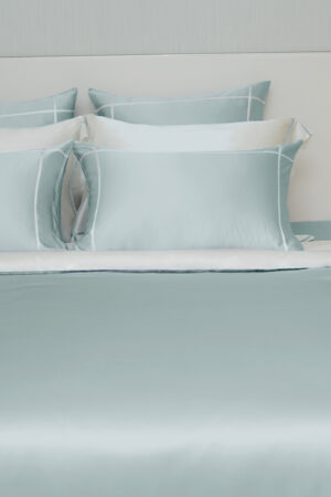 MANITO Fluora Silk Pillowcase Set in mint green and white tones, displayed on a bed with smooth, layered silk fabric.