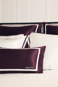 Close-up of MANITO Bordeaux red silk pillowcases with white trim, showcasing intricate craftsmanship.