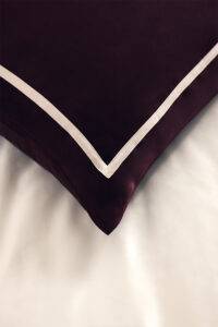 MANITO silk pillow with Bordeaux red fabric and white piping detail.