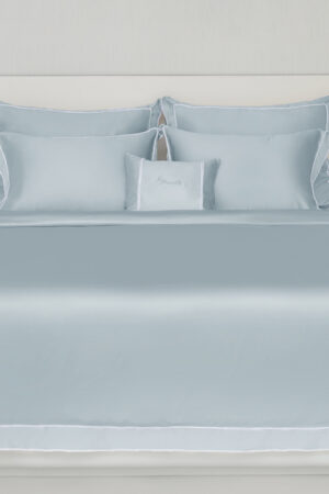 Light blue MANITO Fringe Silk Duvet Cover on a bed with matching pillows, featuring white fringe trims and a minimalist headboard.