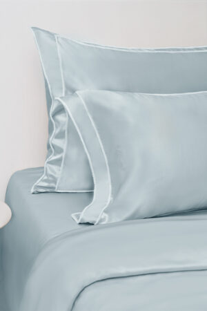 Close-up of a light blue MANITO Fringe Silk Duvet Cover with white fringe trims, emphasizing the smooth silk fabric and plush pillows.