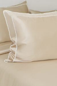 Side angle of a champagne MANITO Fringe Silk Duvet Cover on a bed, displaying white fringe trims.