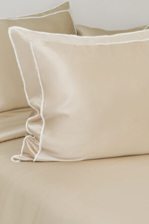 Side angle of a champagne MANITO Fringe Silk Duvet Cover on a bed, displaying white fringe trims.