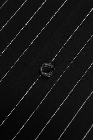 Close-up of black button with MANITO branding on striped silk fabric.